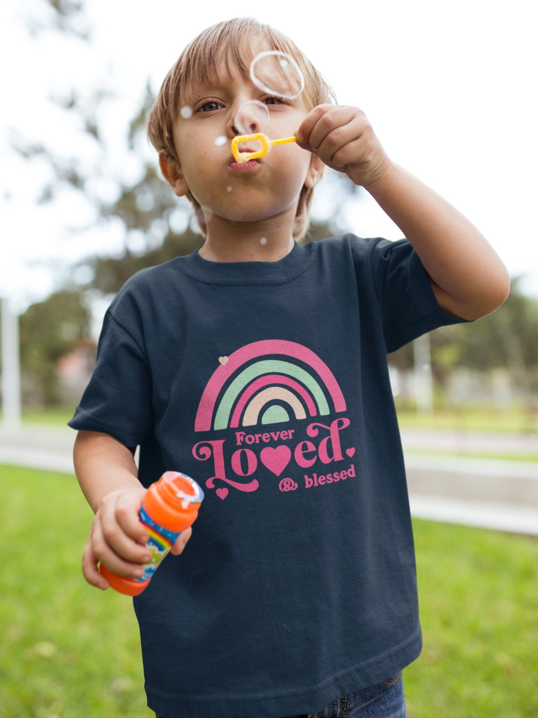 Child wearing a cute rainbow toddler t-shirt blowing bubbles outdoors on a sunny day
