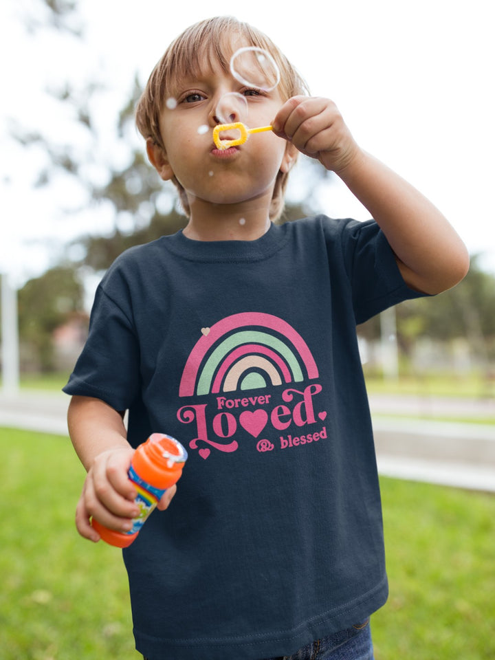 Child wearing a cute rainbow toddler t-shirt blowing bubbles outdoors on a sunny day