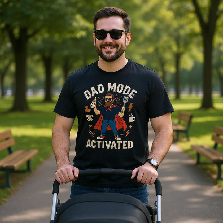 Man wearing black dad mode activated t-shirt by CIASARA pushing a stroller in a park